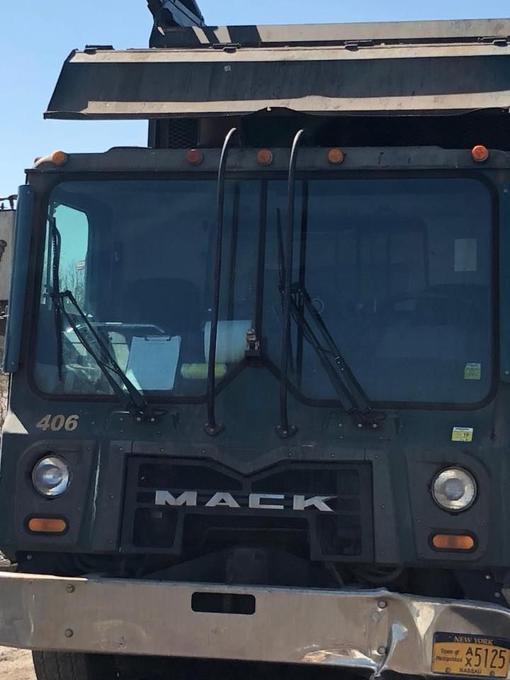 Front view of a dark gray Mack truck with a raised dump bed under a clear sky