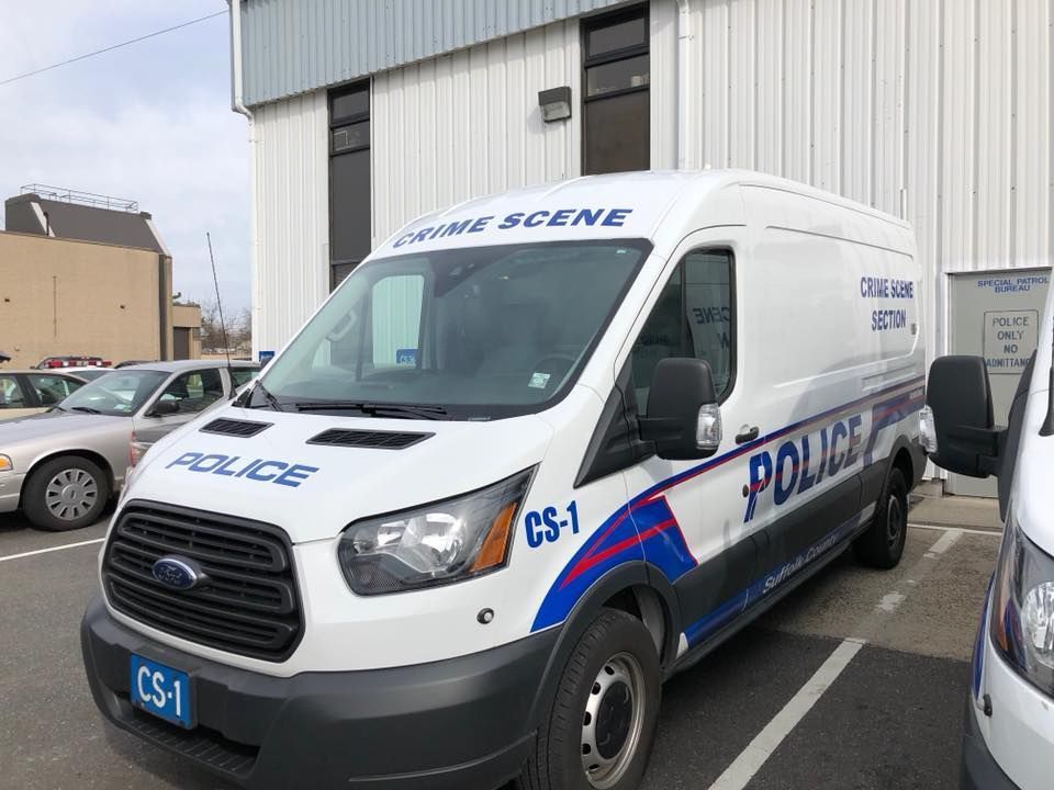 White police van parked outside a building, marked with blue POLICE lettering and red-blue stripes