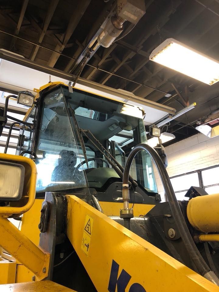 Yellow construction vehicle cab indoors under workshop lights, viewed from the front corner.