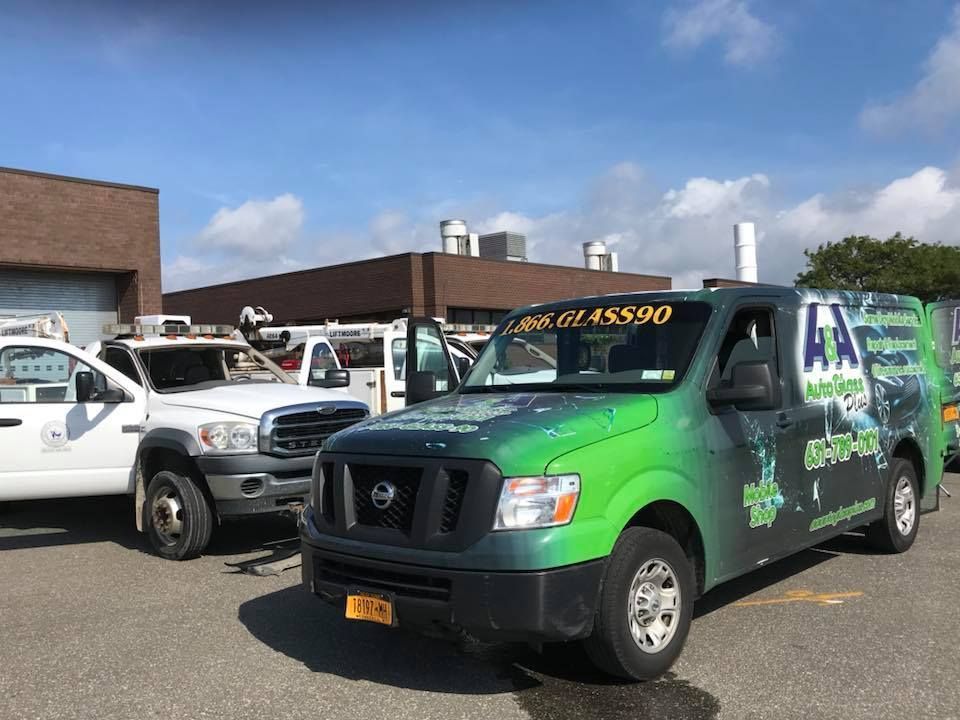 Green-and-black utility van parked in a lot beside a white truck under a blue sky