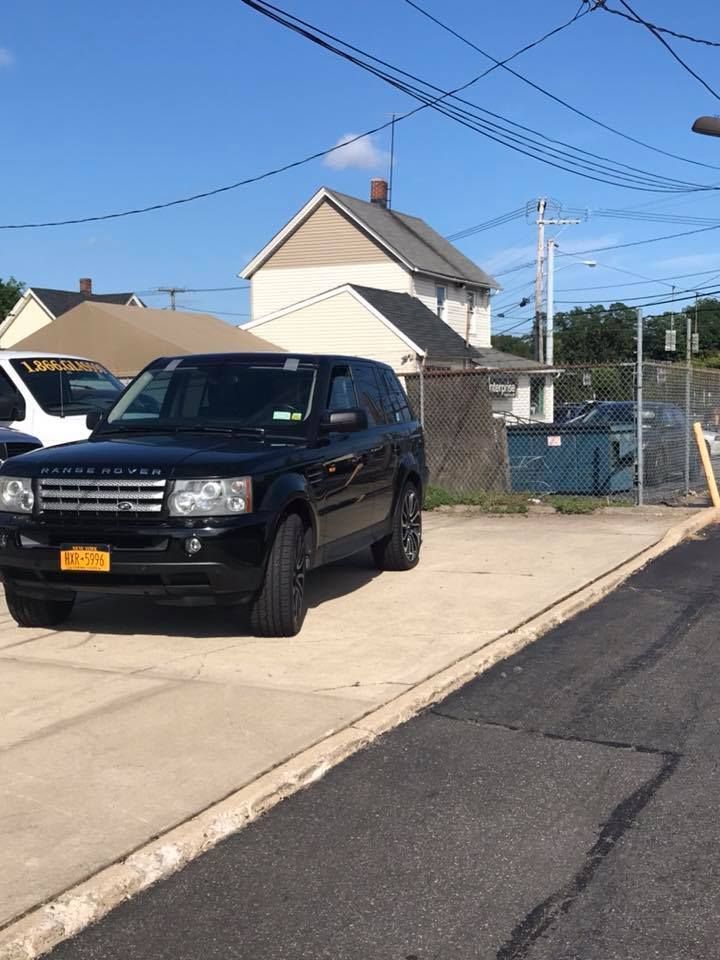 Black SUV parked on a sloped driveway beside a house, with utility wires overhead on a sunny day