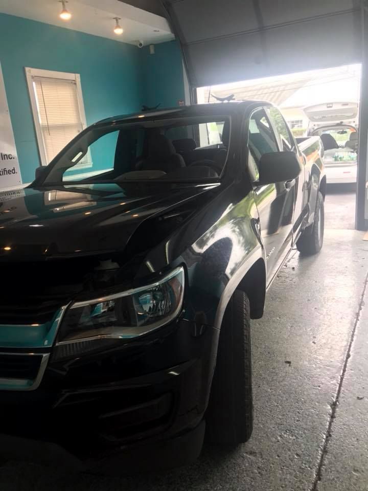 Black pickup truck parked in a garage, with bright daylight coming through the open door.