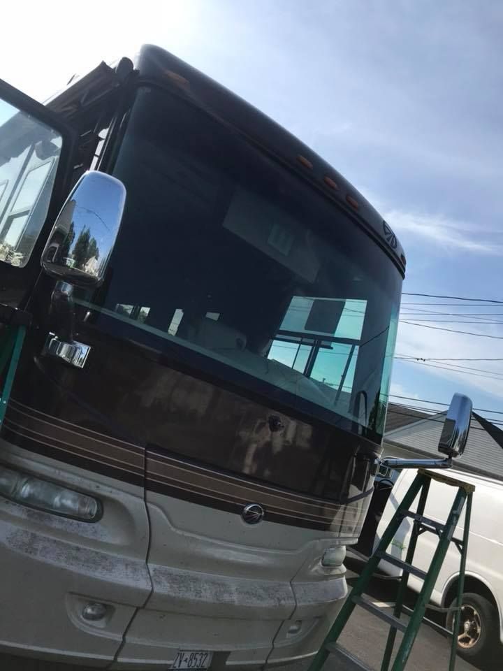 Silver and black coach bus parked outdoors, angled view with blue sky and a white vehicle beside it