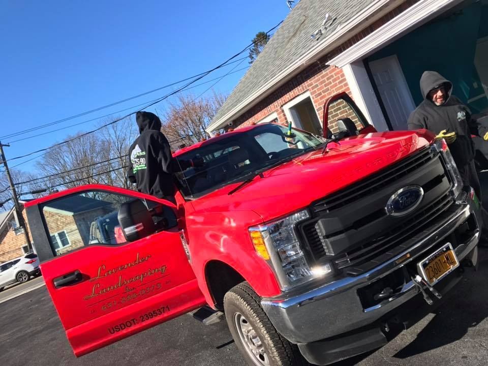 Red pickup truck with open door beside a brick building, two people nearby on a sunny day