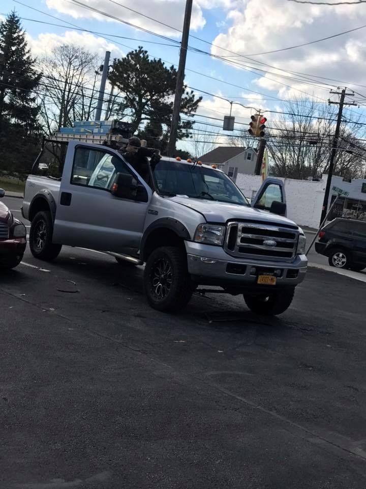 Silver pickup truck parked on a lot with a person in the driver’s seat, under a cloudy sky