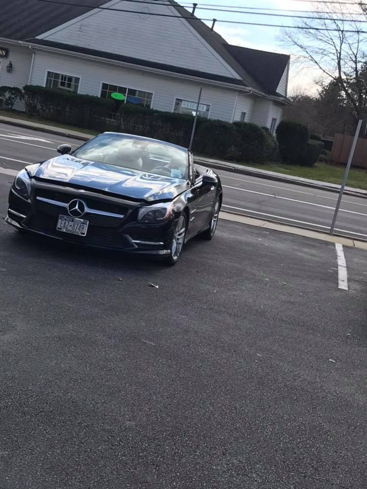 Black Mercedes convertible parked in a lot in front of a house and road.