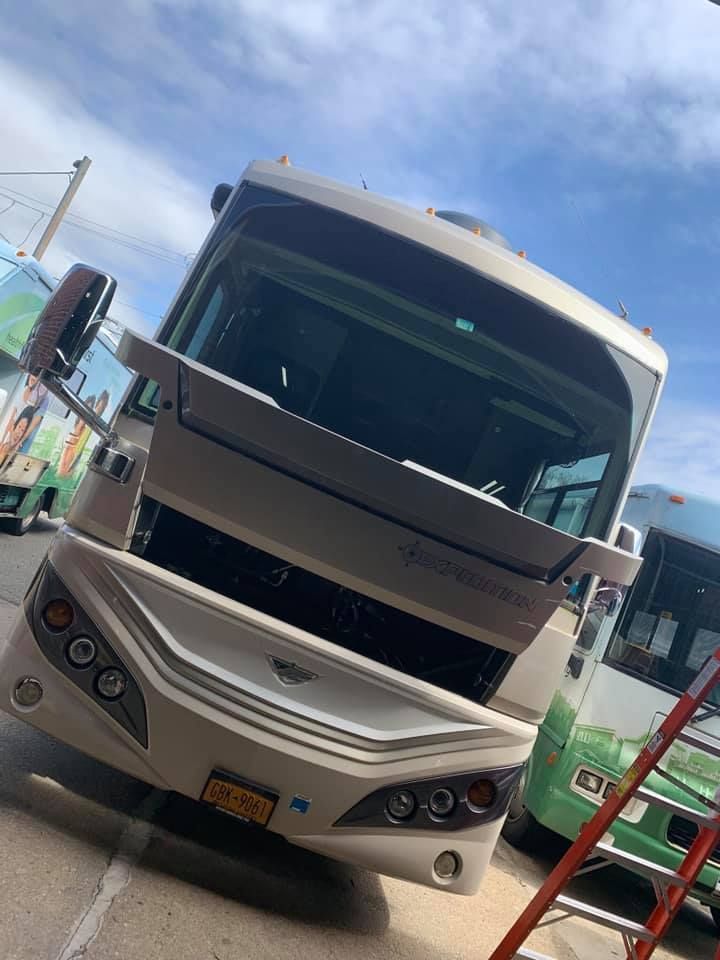 Large white bus parked at a fuel station, angled toward the camera under a blue sky.