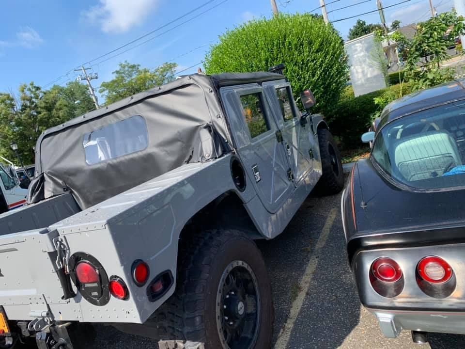 Gray Humvee parked in a lot beside a silver sports car, rear and side view.