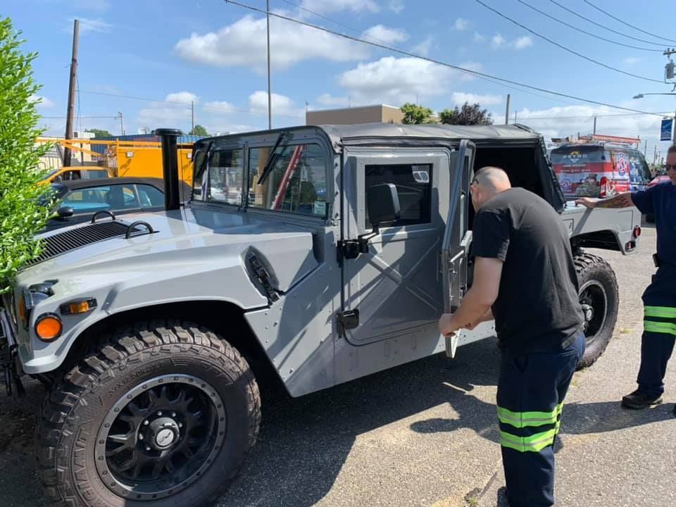 Gray off-road vehicle with open doors, two people standing beside it in a parking lot under a blue sky