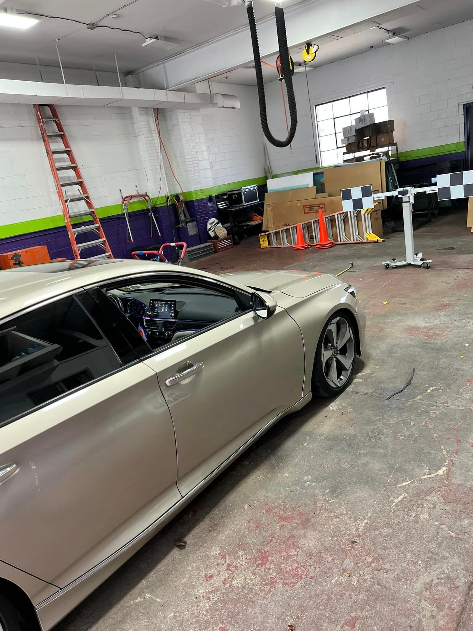 Silver car inside a cluttered auto shop with ladders, tools, and a vehicle lift in the background