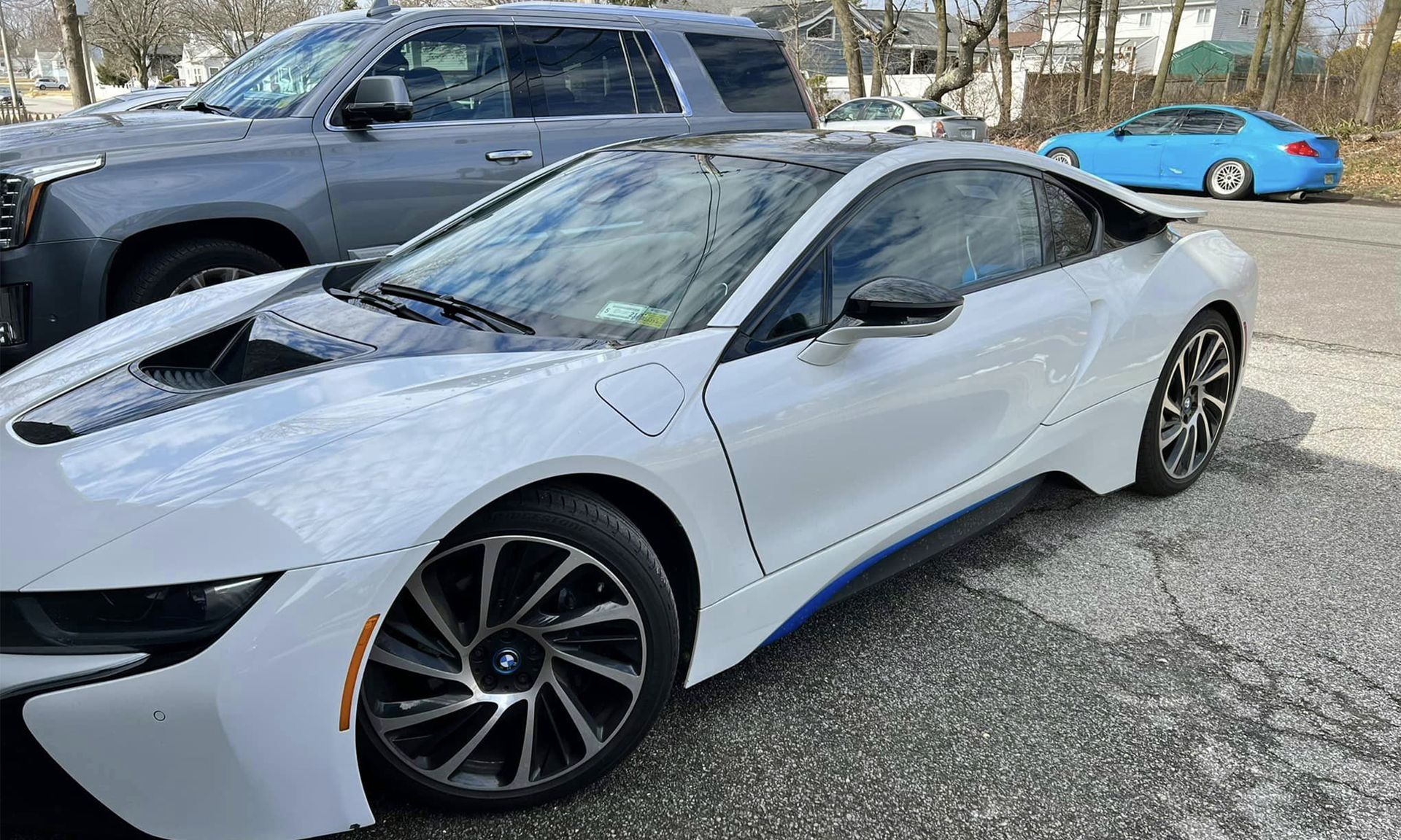 White BMW i8 parked in a lot beside a gray pickup truck and a blue car