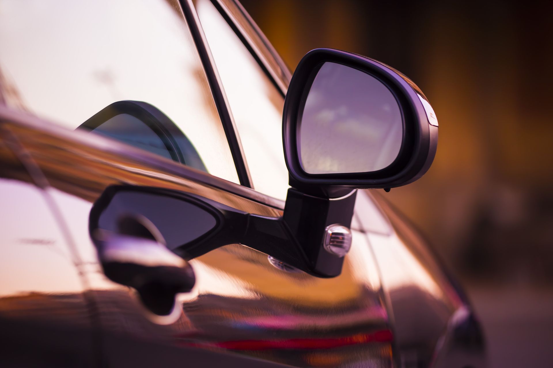 Close-up of a car’s side mirror and door handle reflecting warm sunset light