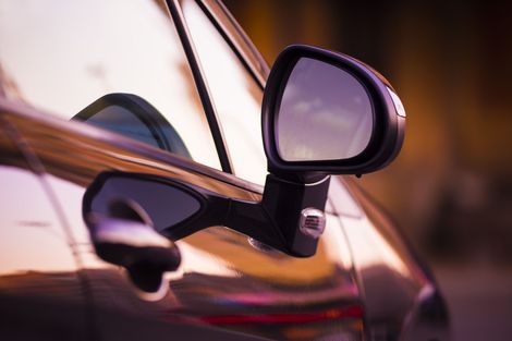 Close-up of a car’s side mirror and door handle reflecting warm sunset light