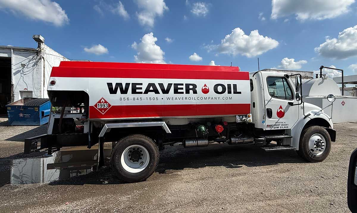 A Weaver Oil fuel truck with a red and white tank parked outdoors on a gravel lot.