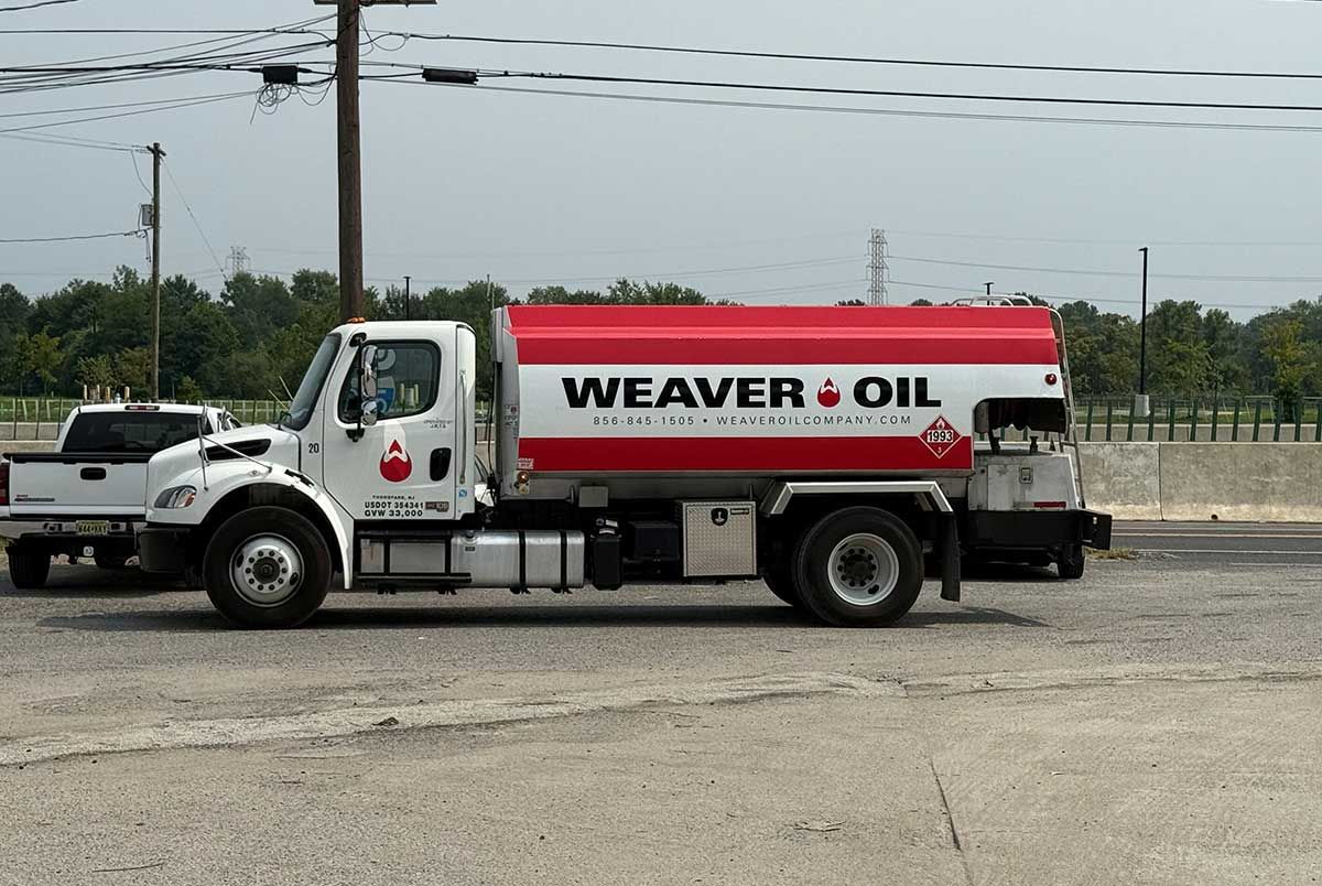 White Weaver Oil truck, red tank, parked on asphalt, overcast sky, with a white truck in the background.