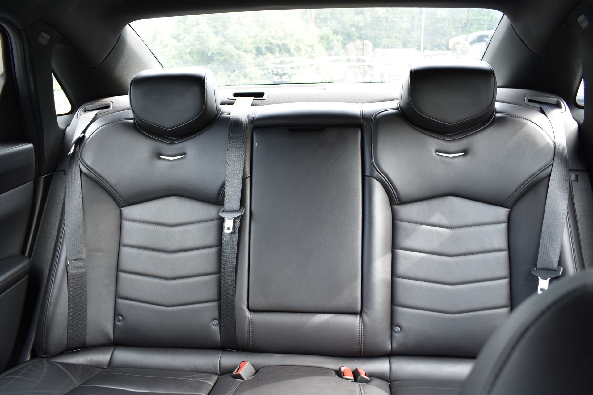 The back seat of a car with black leather seats and seat belts.