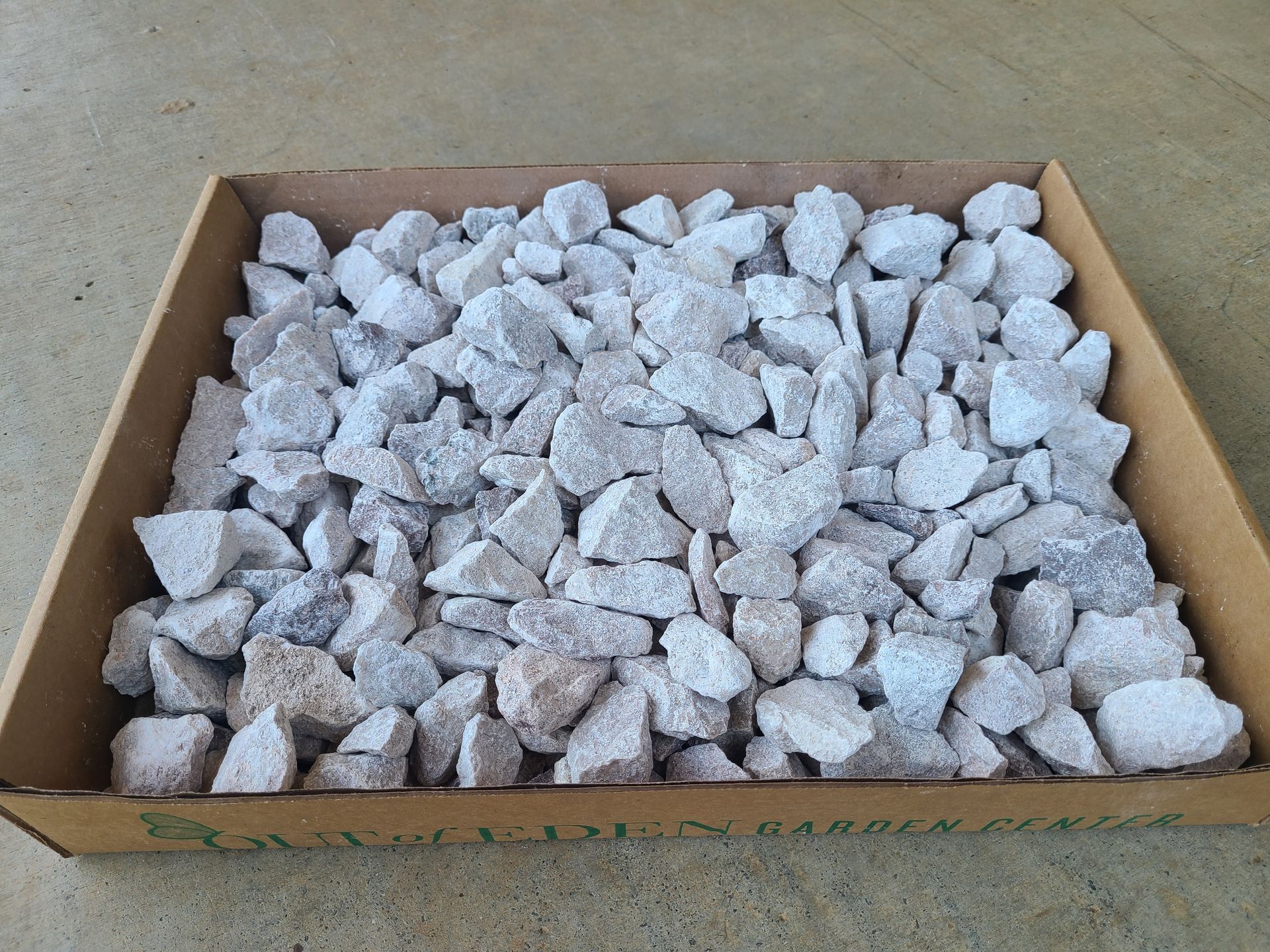 A box filled with white marbles is sitting on a concrete surface.
