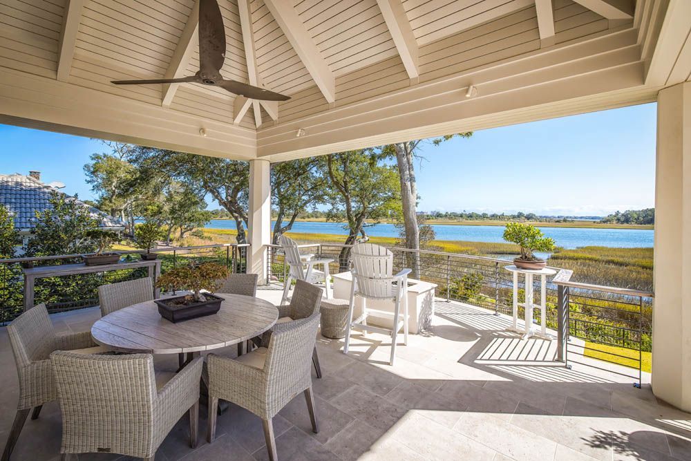 A patio with a table and chairs and a ceiling fan overlooking a body of water.