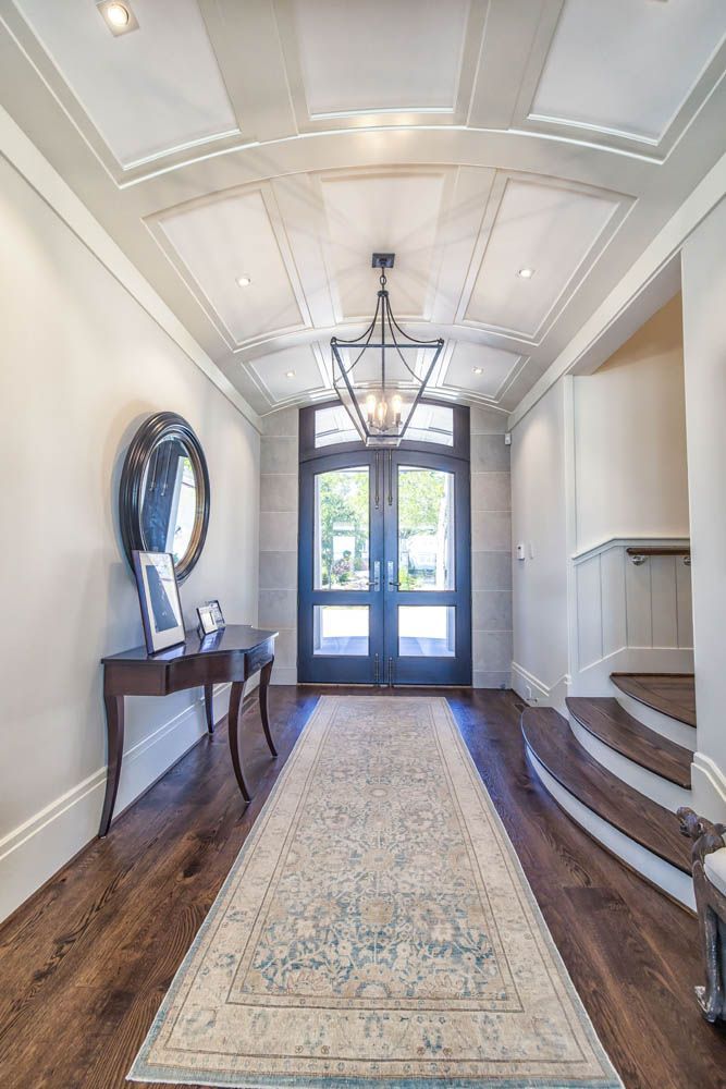 A hallway with a rug, table, mirror and stairs in a house.