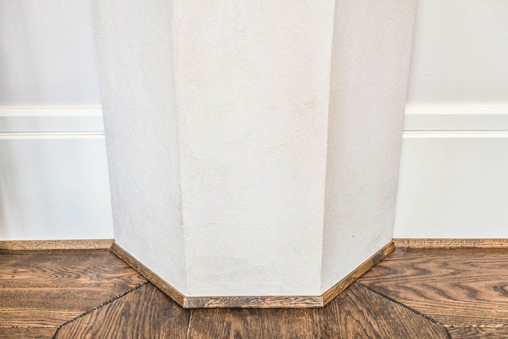 A corner of a room with a wooden floor and a white wall.