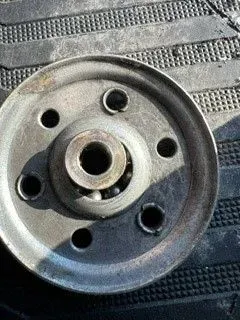 Close-up of a silver metal wheel hub with bolt holes on a textured black surface