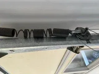 Coiled black spring attached to a garage door track near a pulley mechanism