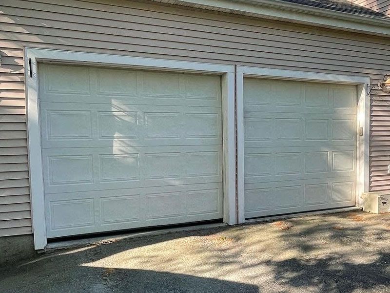 Two white garage doors on a house exterior, with sunlight and shadows on the driveway