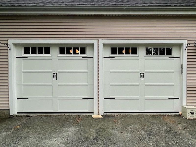 Two white garage doors on a beige house exterior with asphalt driveway in front