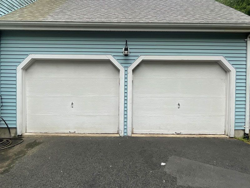 Two white garage doors on a blue house with an asphalt driveway
