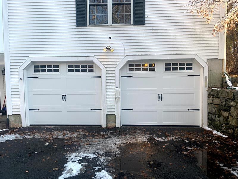 Two white garage doors on a house exterior with blacktop driveway and snow patches nearby