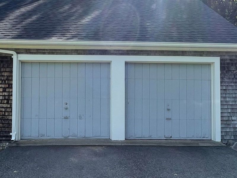 Two gray garage doors with white trim on a house exterior