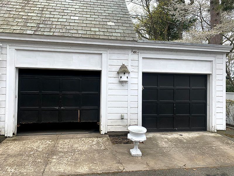 White double garage with black doors, one open, on a concrete driveway with a birdbath in front.