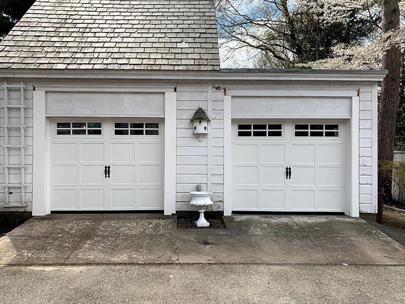 Two white garage doors on a house exterior with a small lantern and bench between them