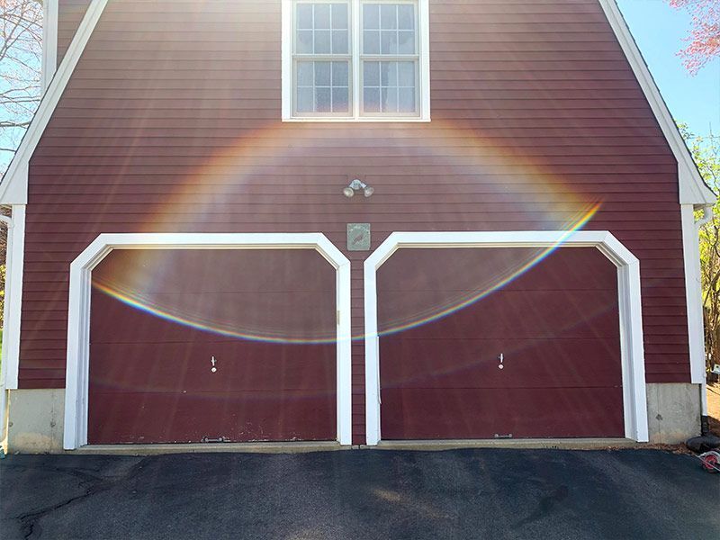 Red two-car garage with white trim and a window above the doors in bright sunlight.