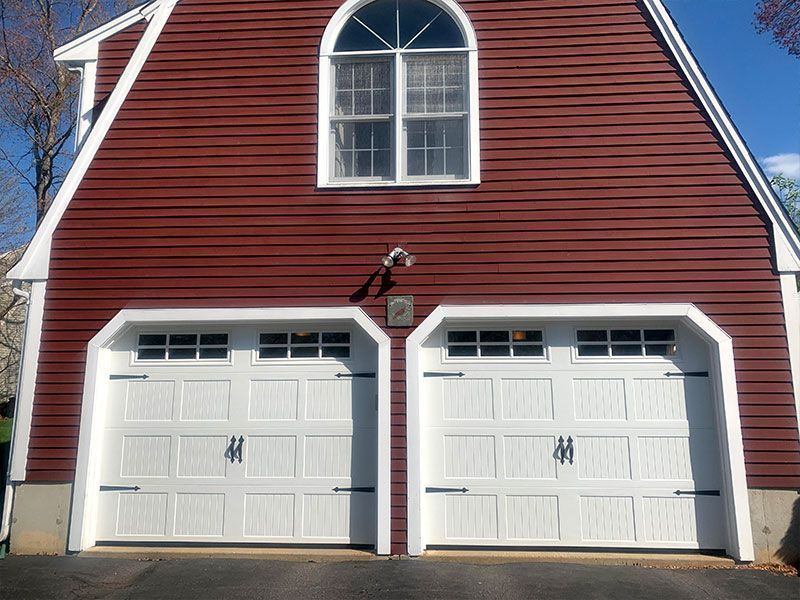 Red barn-style garage with two white doors and a large arched window above them.