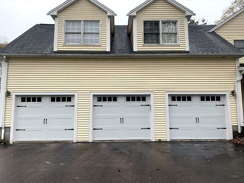 Three beige garage doors on a townhouse with two dormer windows above