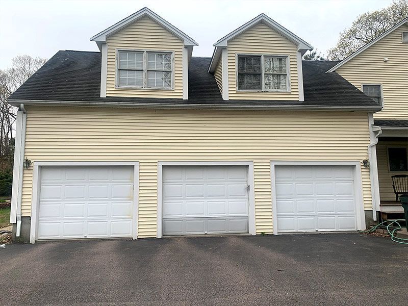 Three-car beige garage with white doors and dormer windows on a driveway