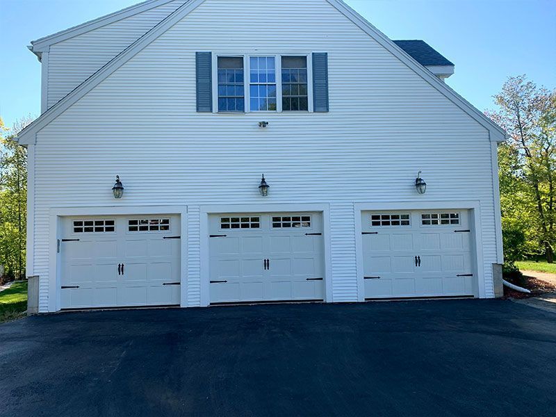 White three-bay garage with a window above, set behind a paved driveway.