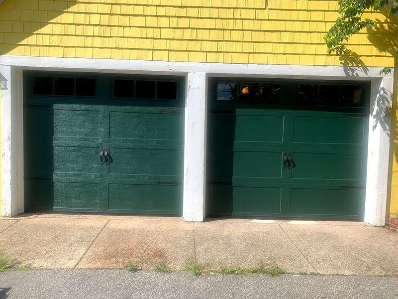 Two dark green garage doors beneath a yellow brick facade with white pillars