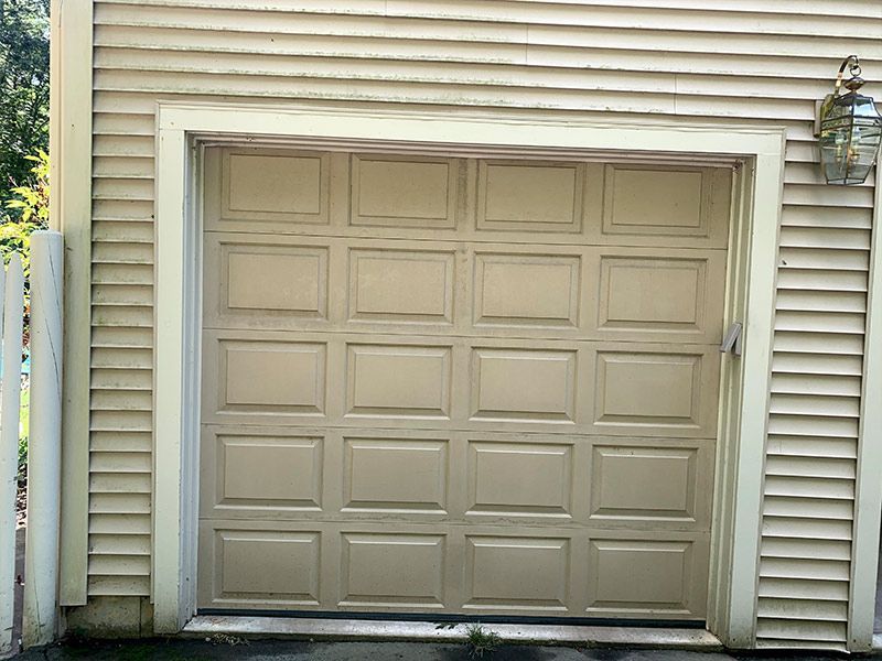 Beige garage door on a house exterior, framed by white trim and light gray siding.