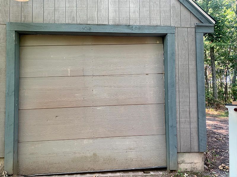 Closed tan garage door on a weathered gray shed exterior