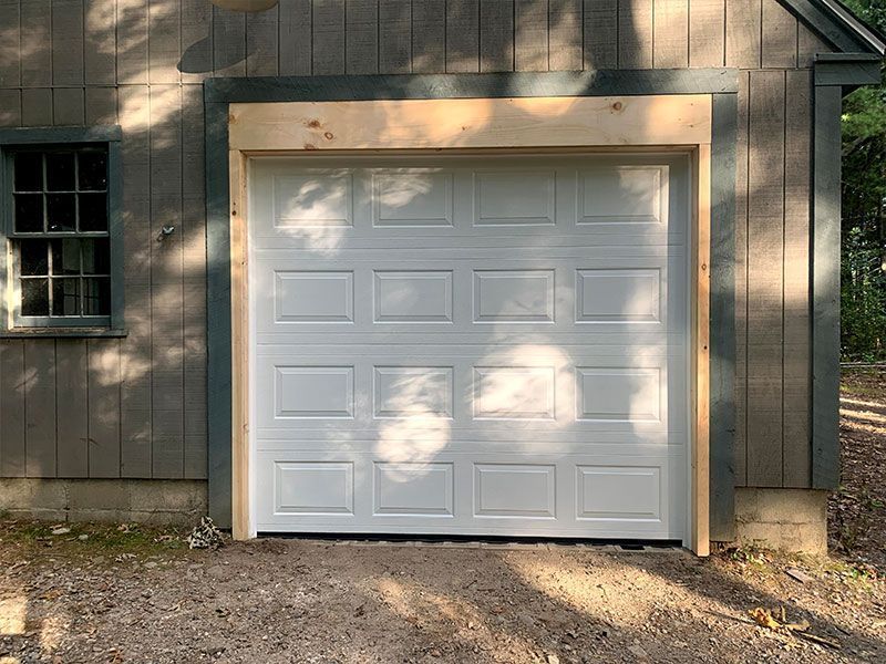 White garage door on a brown house exterior with sunlight and tree shadows.