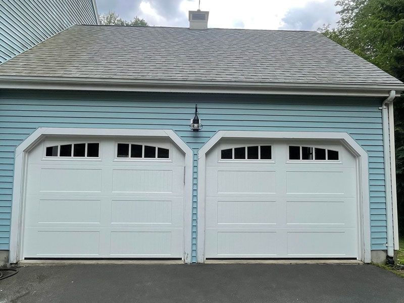 Two white garage doors on a blue-sided house with gray shingled roof