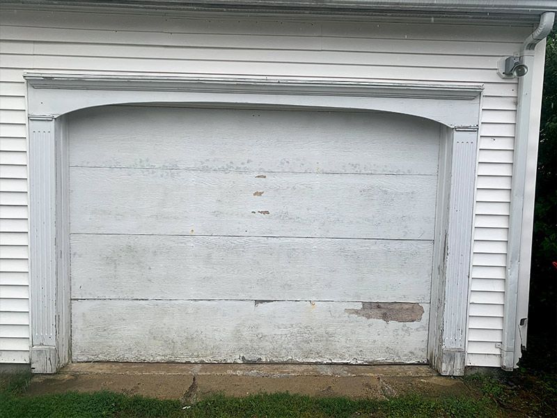 Closed white garage door with worn paint and a small damaged area at the bottom right