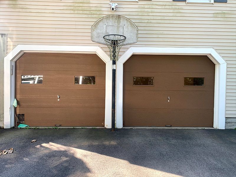 Two brown garage doors with basketball hoop mounted between them on a beige house exterior