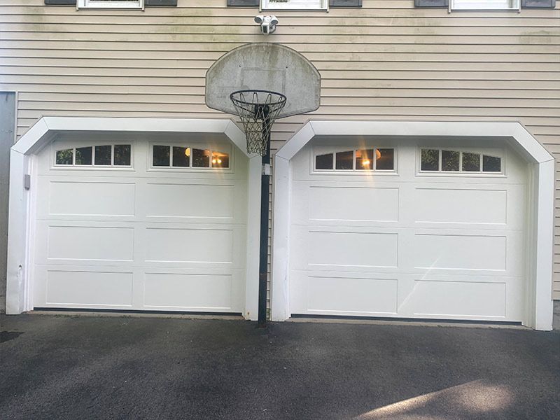 Two white garage doors on a beige house with a basketball hoop above them.