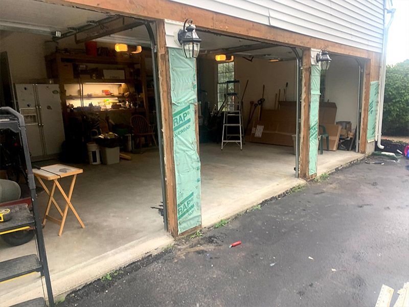 Open garage with workshop clutter, green doors, ladder, and wet driveway beside a house