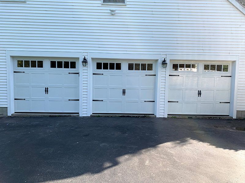 Three white garage doors on a white house exterior with dark driveway pavement in front