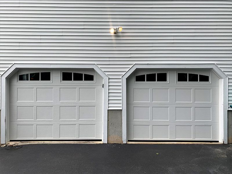 Two white garage doors on a gray house exterior with black asphalt driveway