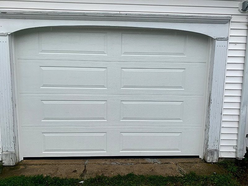 White two-car garage door under a gray house eave, viewed from outside.